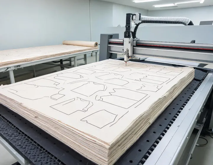 Vacuum CNC fabric cutting table with nested marker and multi-ply stack in an apparel cutting room